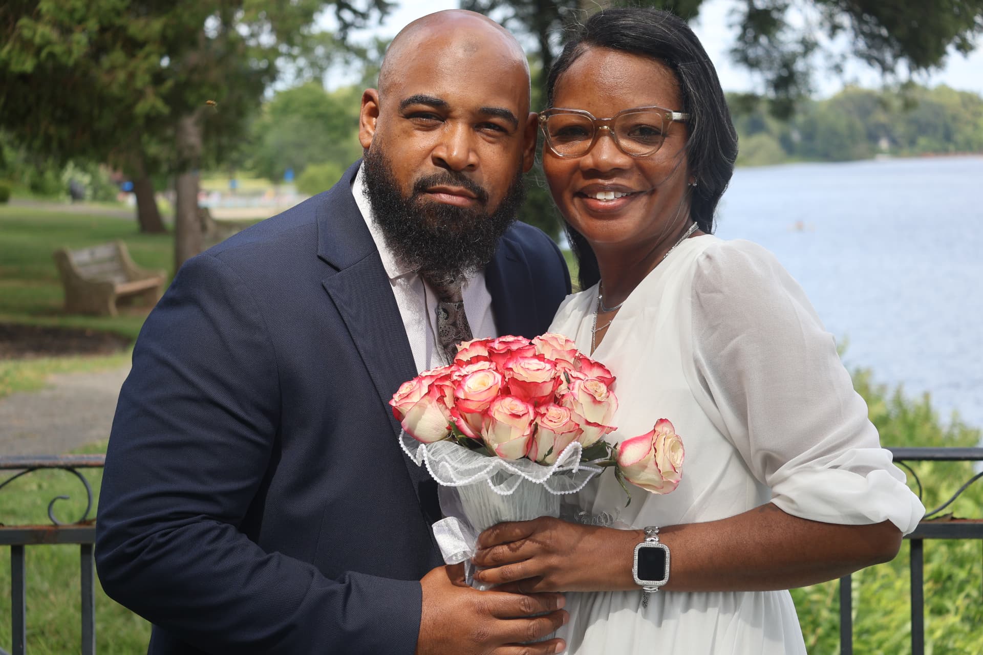 Newlyweds holding pink roses beside a lake after their ceremony
