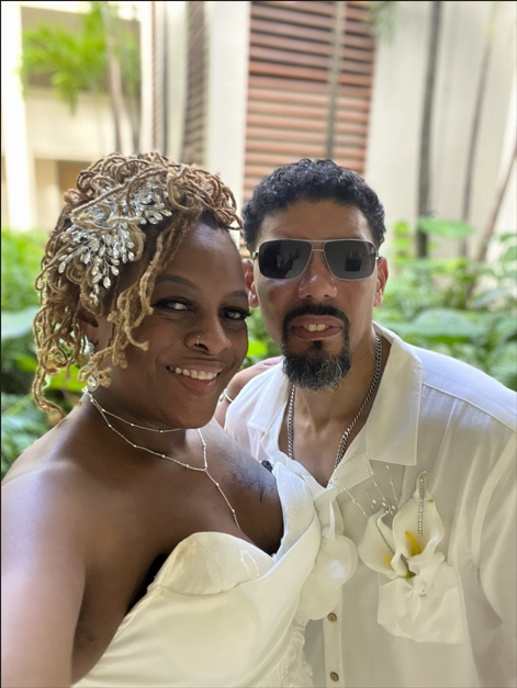 Kesha and her husband, Neil, dressed in white, standing close together and smiling.